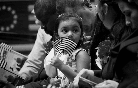 Young girl in a crowd waving a small US flag.